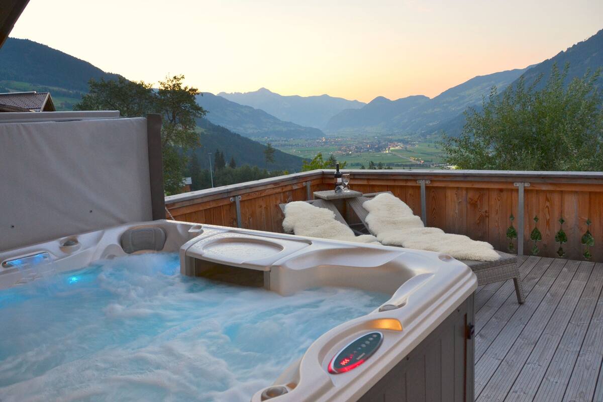 A hot tub with a wooden deck and a scenic mountain view.
