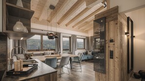 Une cuisine moderne avec des poutres en bois, un coin repas avec des chaises et une vue sur la campagne grâce à de grandes fenêtres.