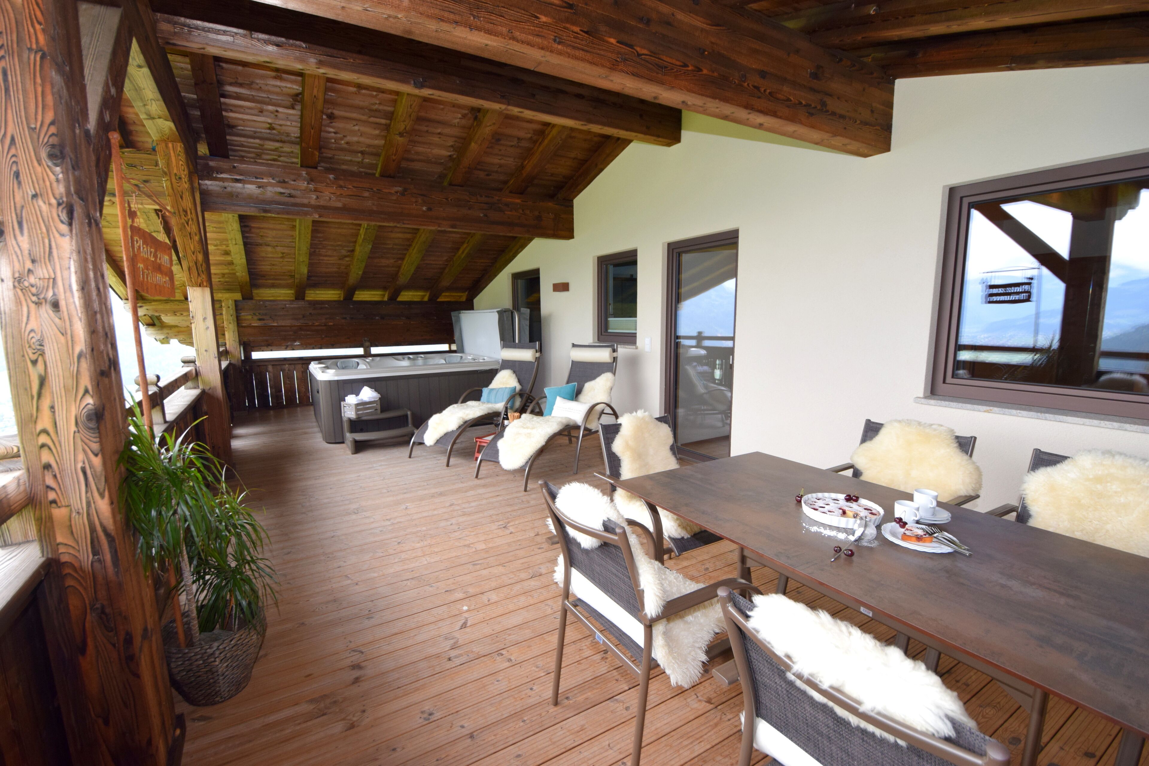 A wooden deck with a dining table and chairs, a hanging plant, and a view of the mountains.