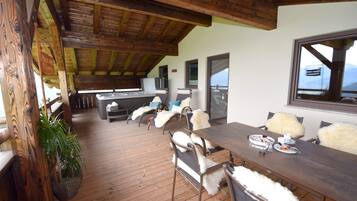 A wooden deck with a dining table and chairs, a hanging plant, and a view of the mountains.