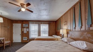 Ein Hotelzimmer mit Holzvertäfelung, zwei Betten, einem Deckenventilator und einem Fenster mit Jalousien.