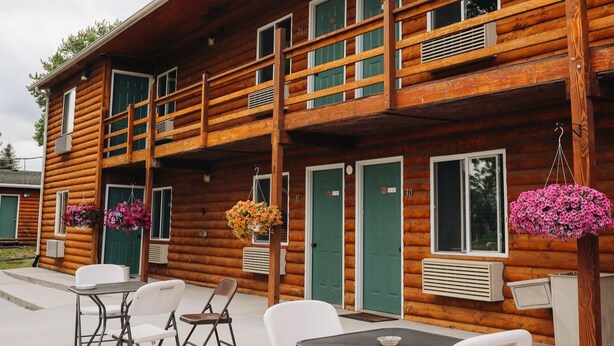 Eine Holzdiele mit Balkon, Sitzgelegenheit im Freien und hängenden Blumenkörben.