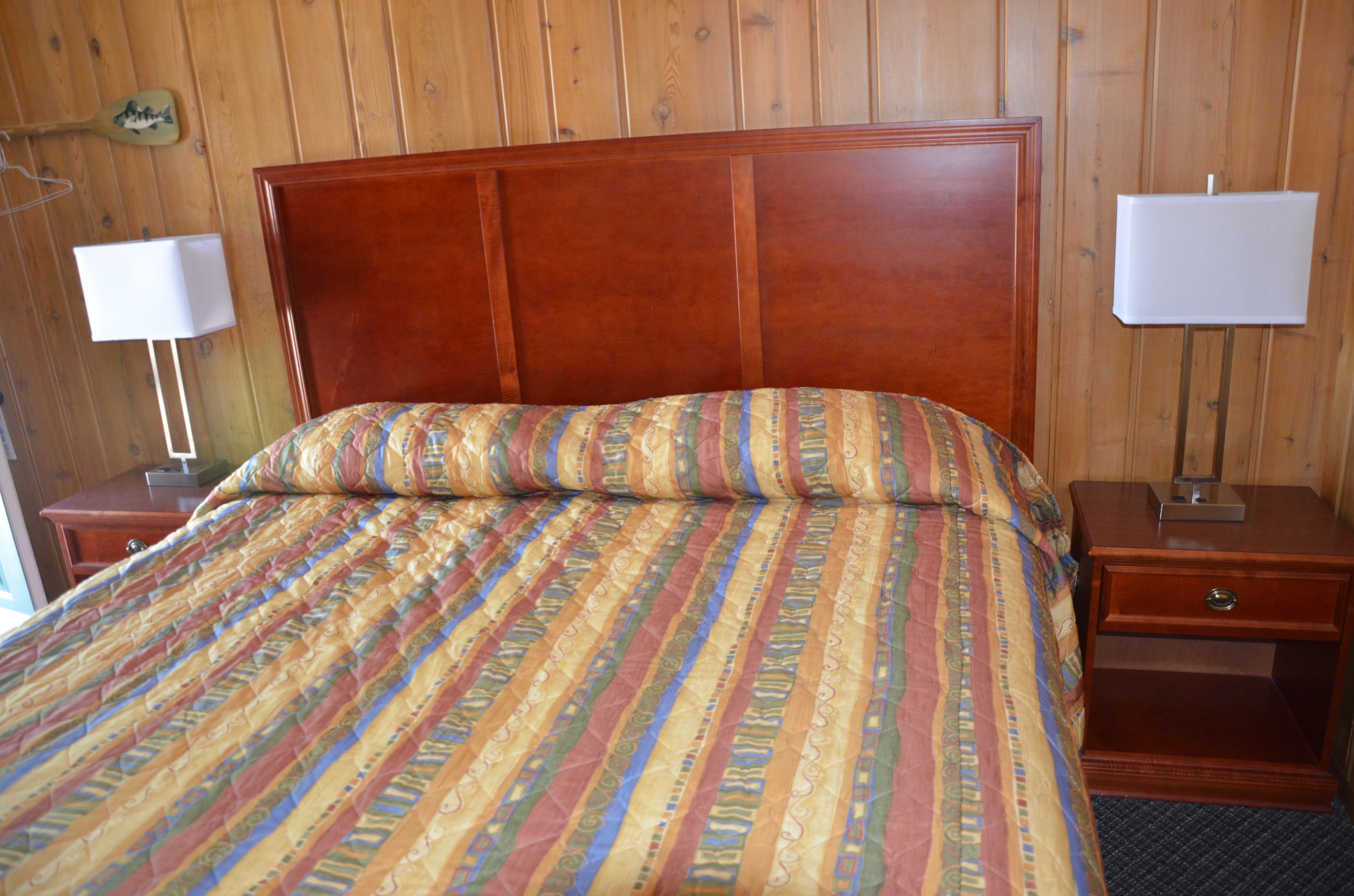 Ein Zimmer mit Holzwänden, einem Bett, zwei Nachttischen und zwei Wandlampen.