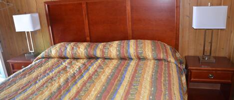 Habitación con paneles de madera, una cama, dos mesitas de noche y dos lámparas de pared.