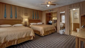 Ein Hotelzimmer mit zwei Betten, einem Deckenventilator, einem kleinen Tisch und einem durch eine offene Tür einsehbaren Badezimmer.