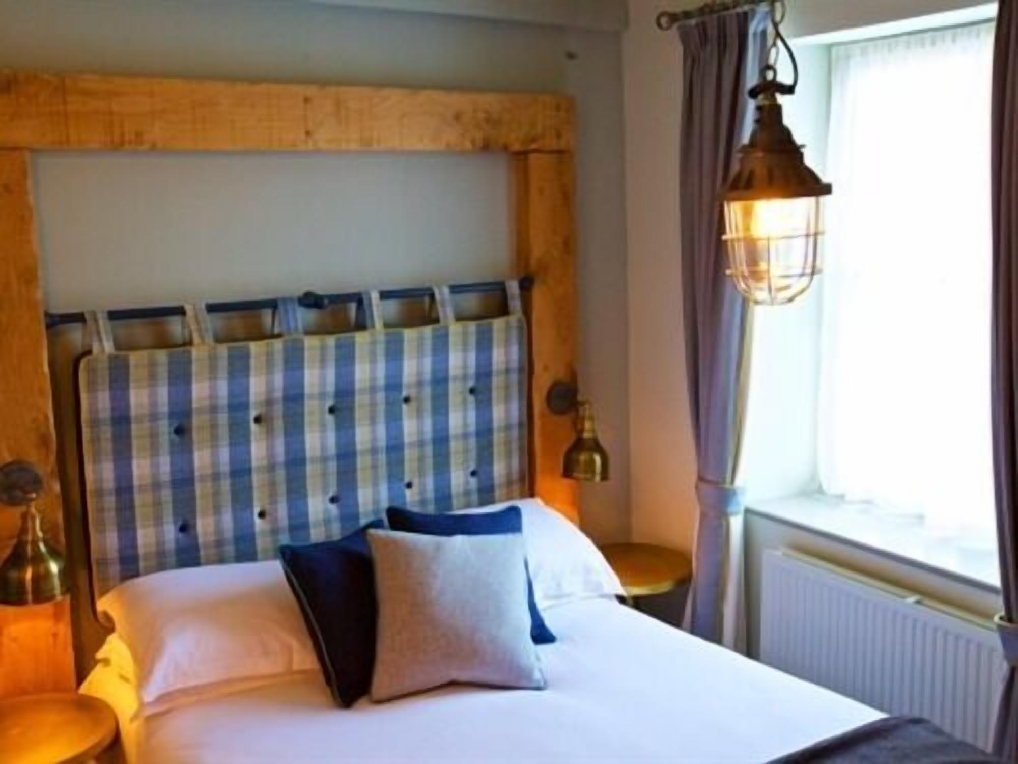 A bed with a plaid headboard, a bedside lamp, and a window with curtains.