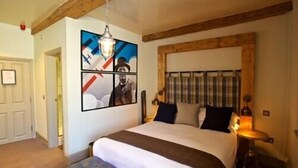 Une chambre à coucher avec un grand lit, un banc, une tête de lit agrémentée de rideaux, un luminaire suspendu et un mur décoré de tableaux encadrés.