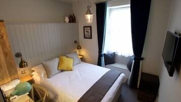Una habitación de hotel con cama, mesita de noche, lámpara y televisión.