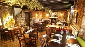 Un restaurant avec des tables et des chaises en bois, des murs en pierre et des plantes suspendues.