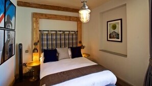 Une chambre avec un plafond en bois, un lit doté d’une tête de lit à rayures, une lampe de chevet et un tableau encadré accroché au mur.