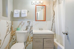 A bathroom with a toilet, sink, and mirror. There are towels hanging on the wall and a shower curtain.