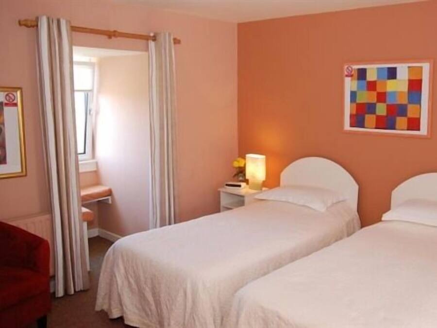 Habitación de hotel con dos camas, una mesita de noche con lámpara, una obra de arte colorida en la pared y una silla roja.