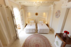 Habitación de hotel con dos camas, una araña, un adorno con forma de sol en la pared y una mesita con un florero.