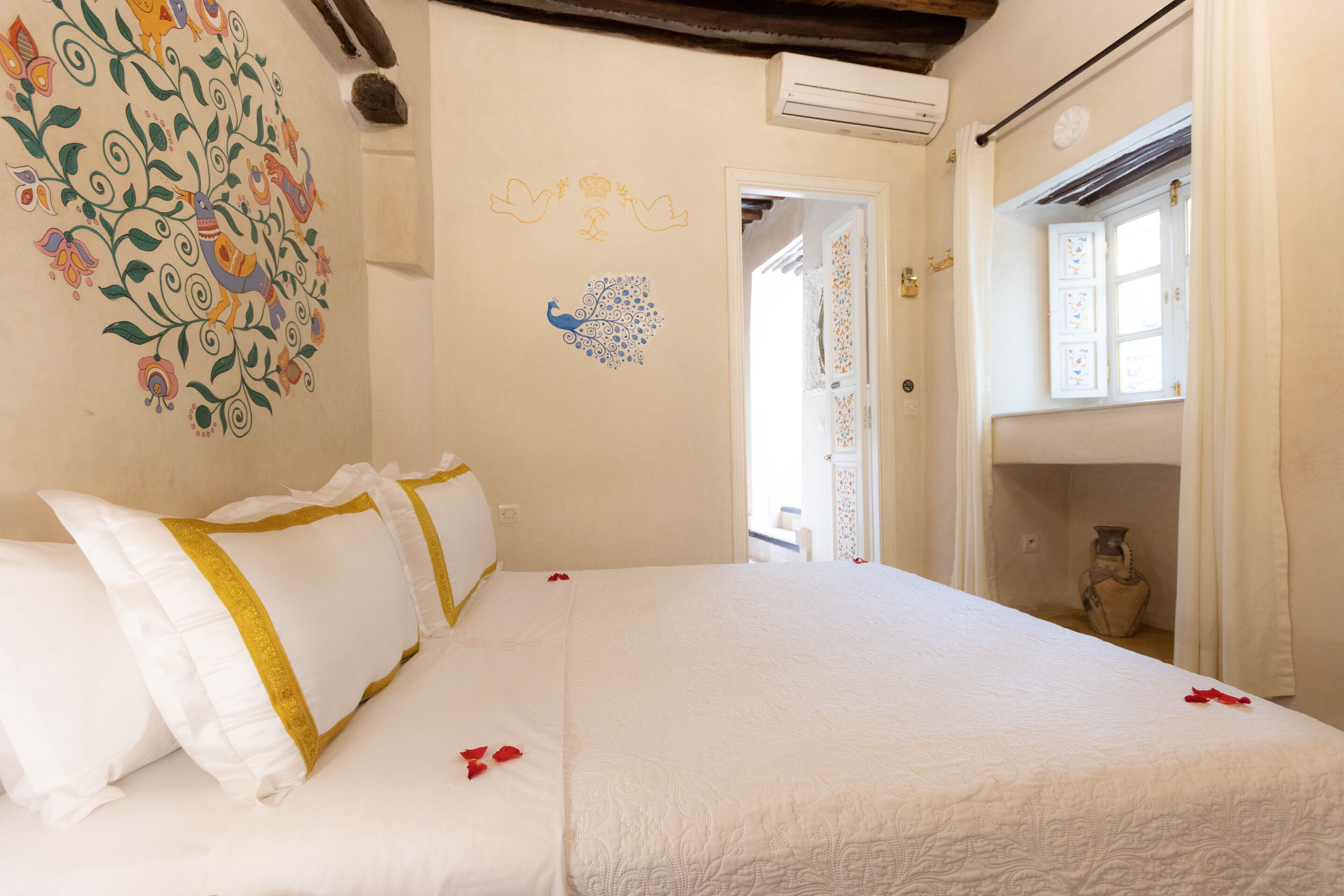 Une chambre d’hôtel avec un grand lit, du linge de lit blanc, des œuvres d’art décoratives au mur et une fenêtre avec des rideaux.