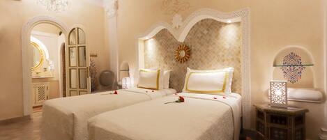 A hotel room with two beds, a chandelier, a decorative mirror, and a small side table.