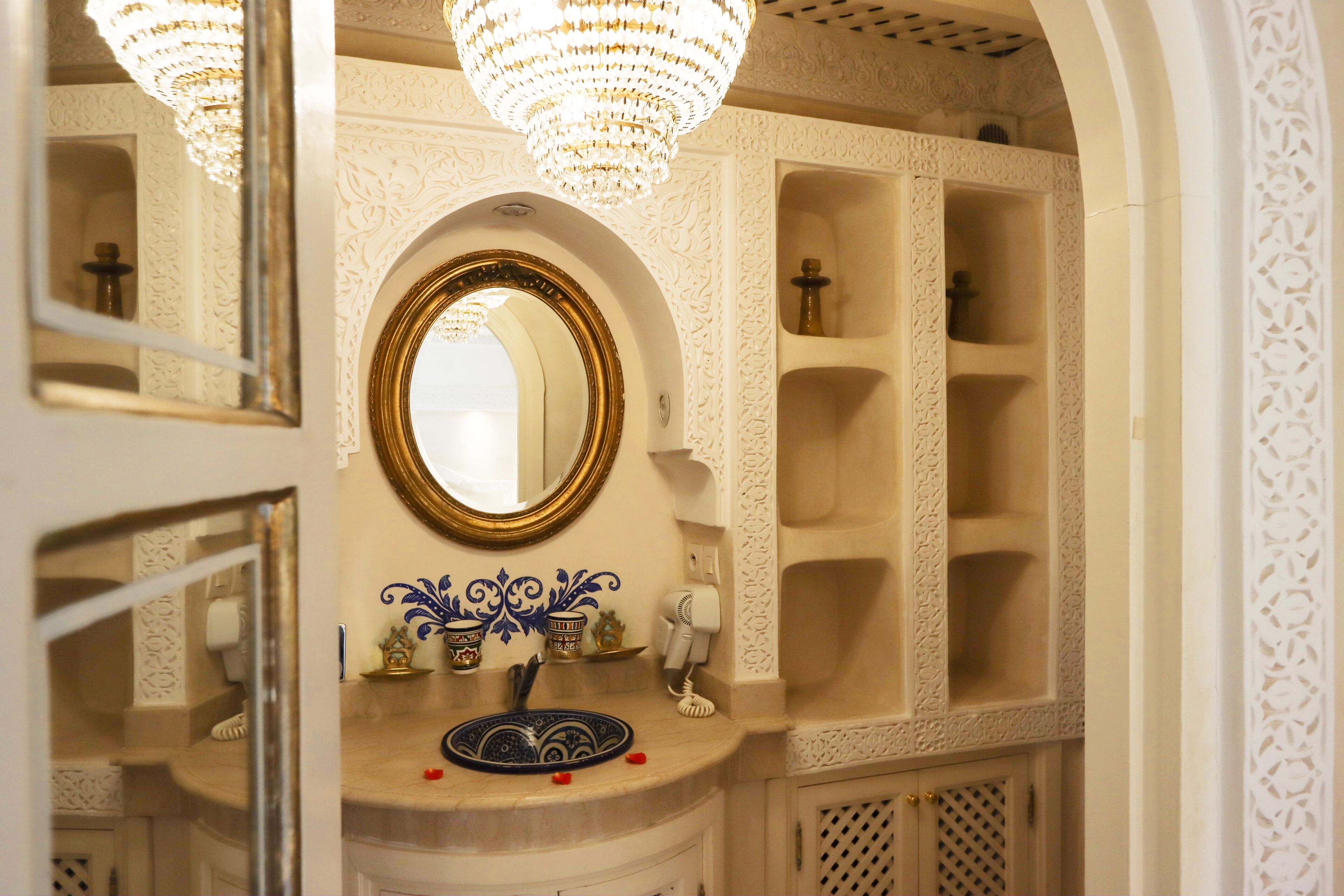 An ornate bathroom with a gold-framed mirror, decorative tiles, and a chandelier.