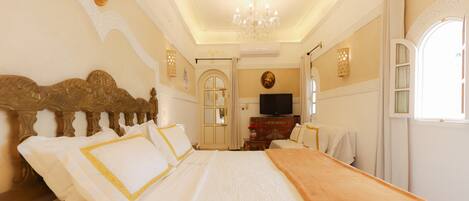 A spacious bedroom with a large bed, ornate headboard, and a chandelier.