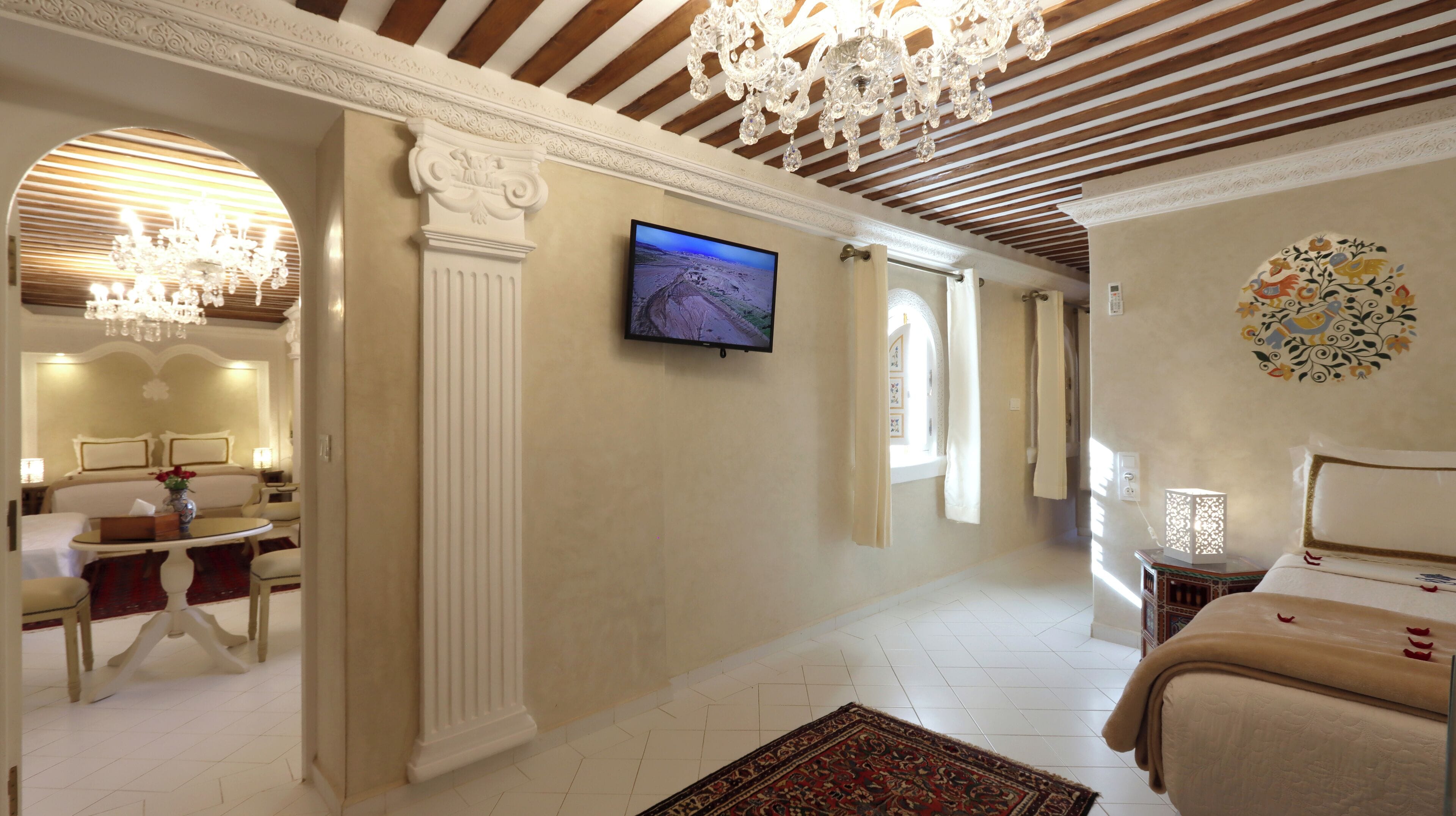 Una habitación de hotel con cama, televisión, candelabro y un adorno en la pared.
