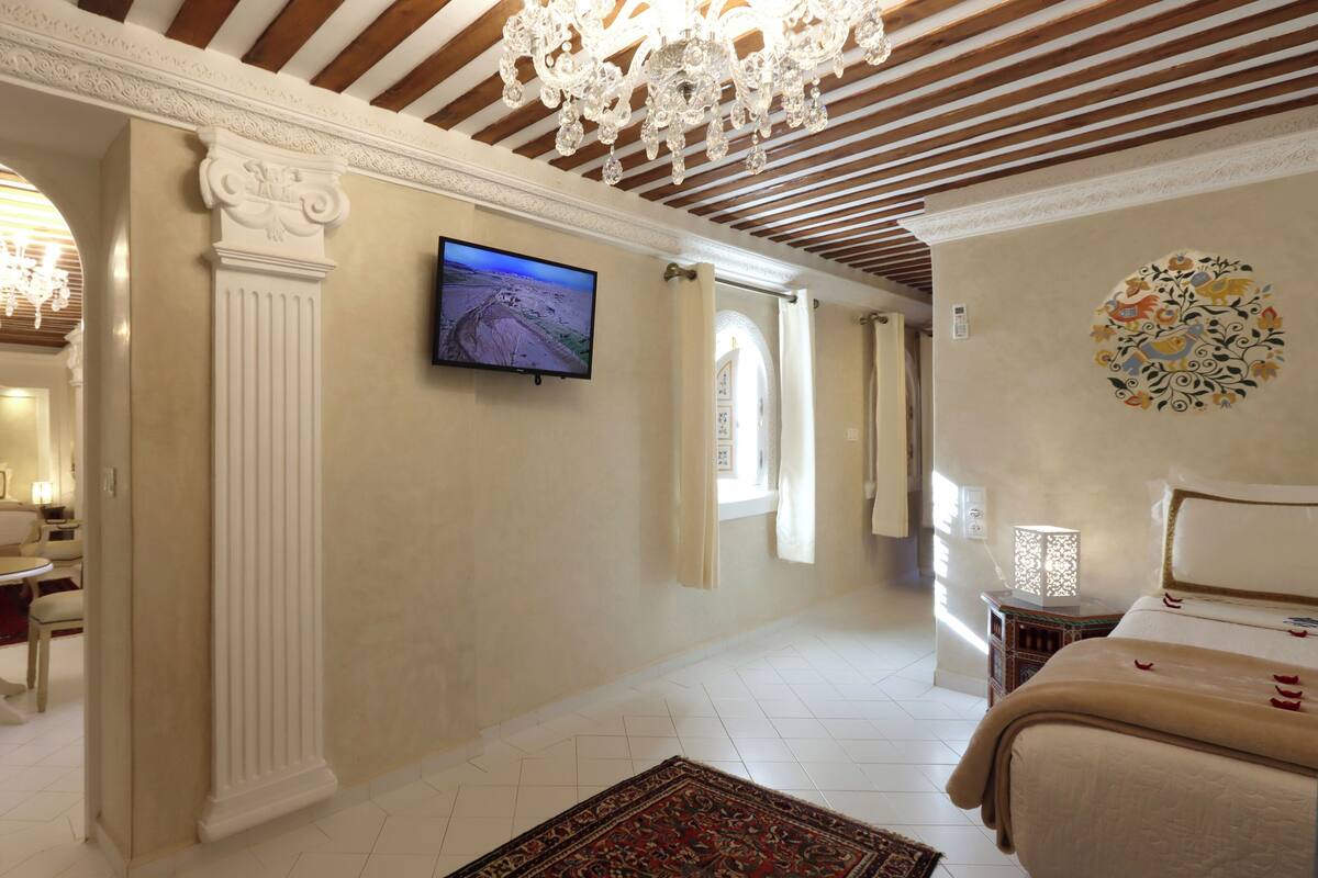 Una habitación de hotel con cama, televisión, candelabro y un adorno en la pared.