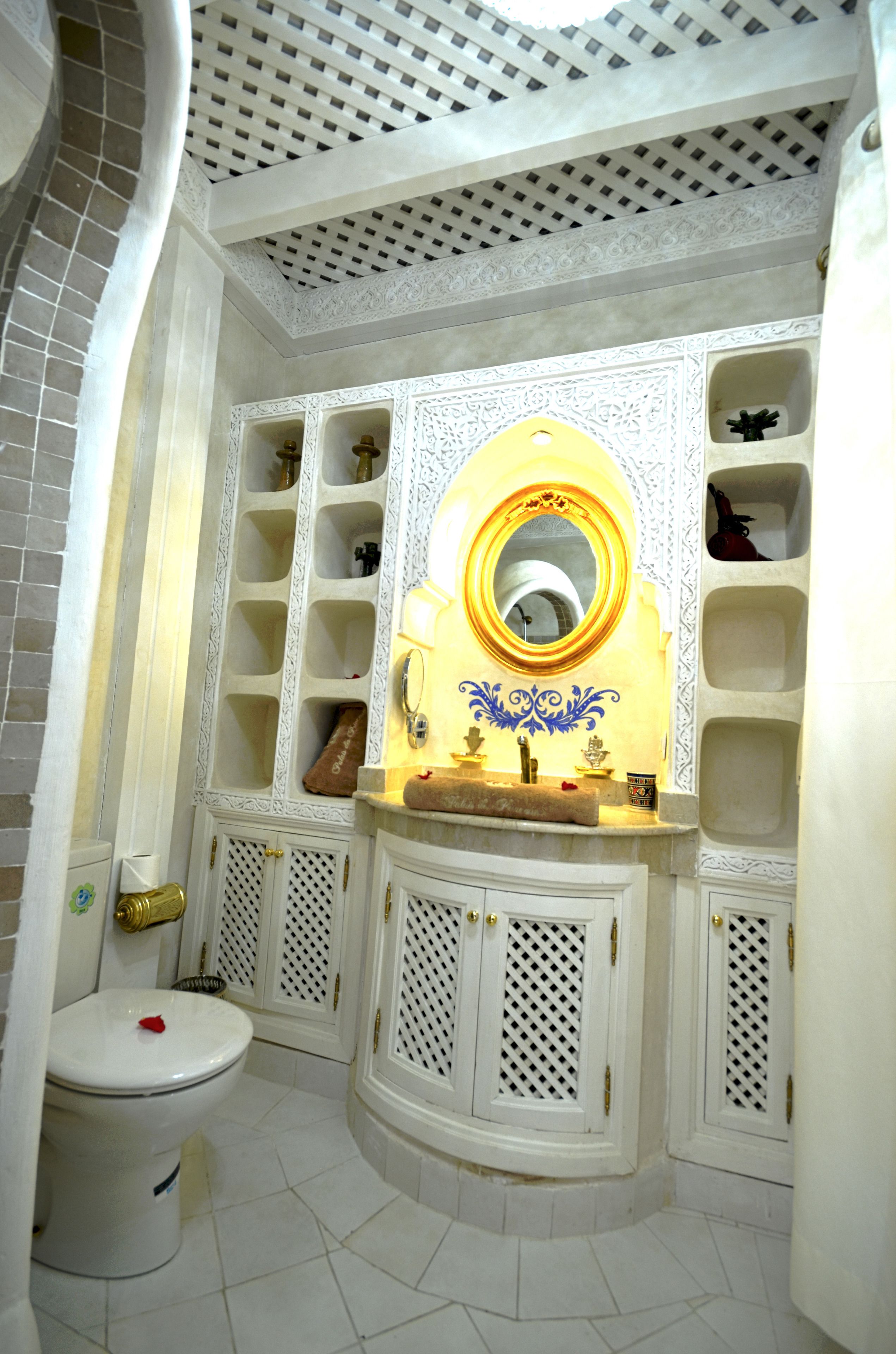 A bathroom with a white toilet, a sink with a gold mirror, and decorative shelves.