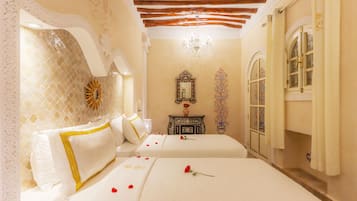 Een hotelkamer met twee bedden, een kroonluchter, een decoratieve spiegel en een bloemarrangement.