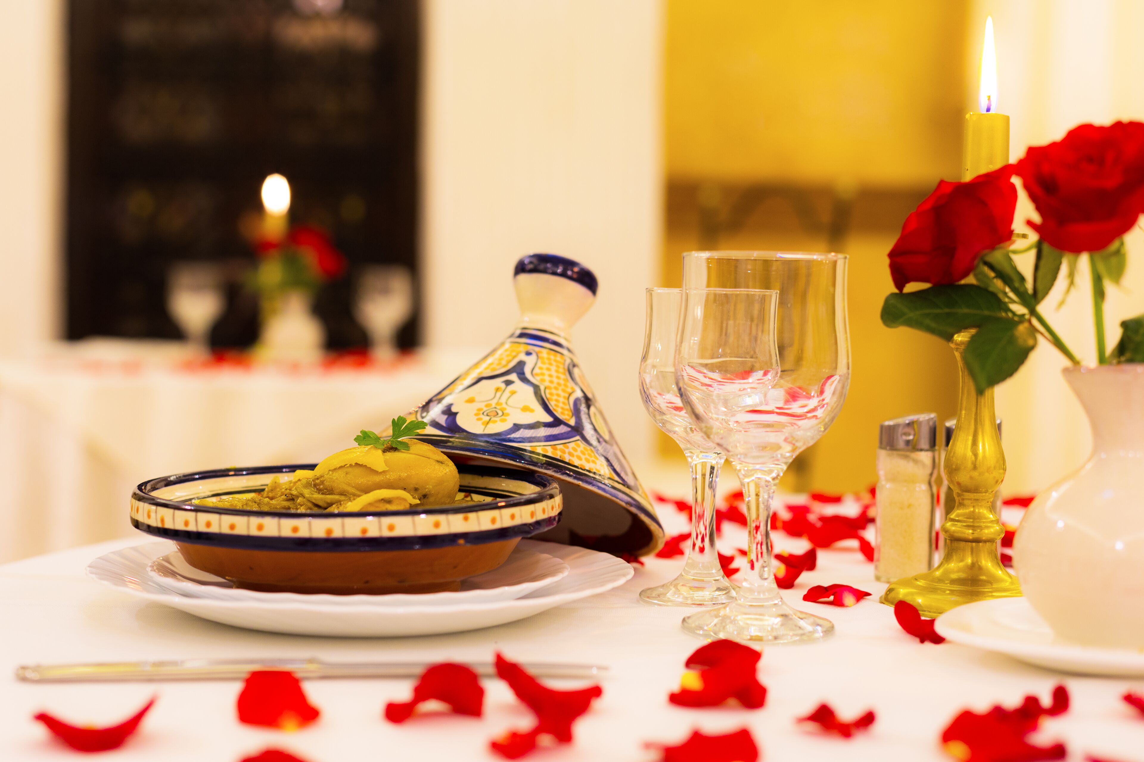 A dining table with a Moroccan tagine, a glass, and a candle.