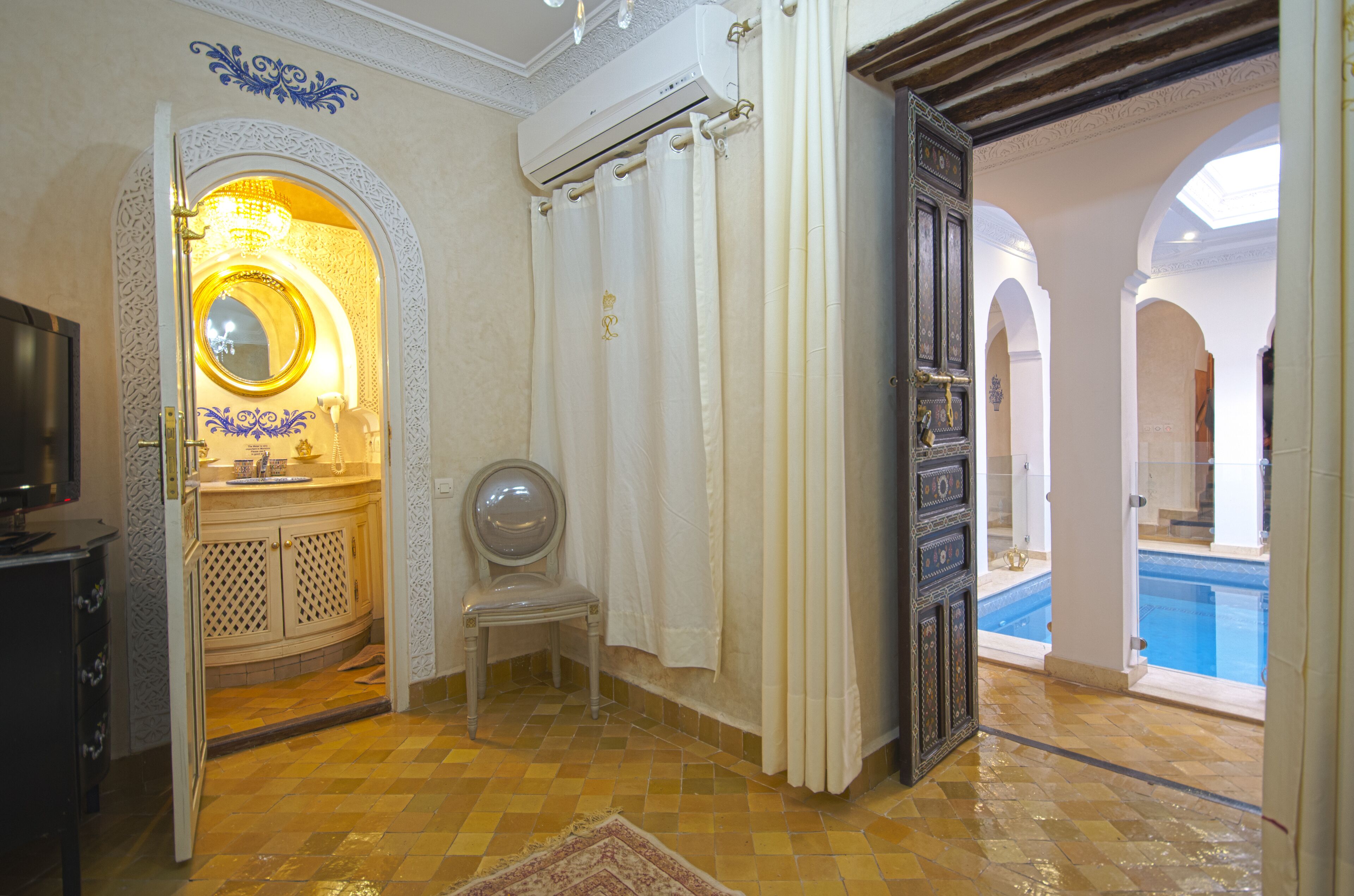 A bathroom with a mirror, sink, and shower curtain. There is a chair and a pool visible in the background.