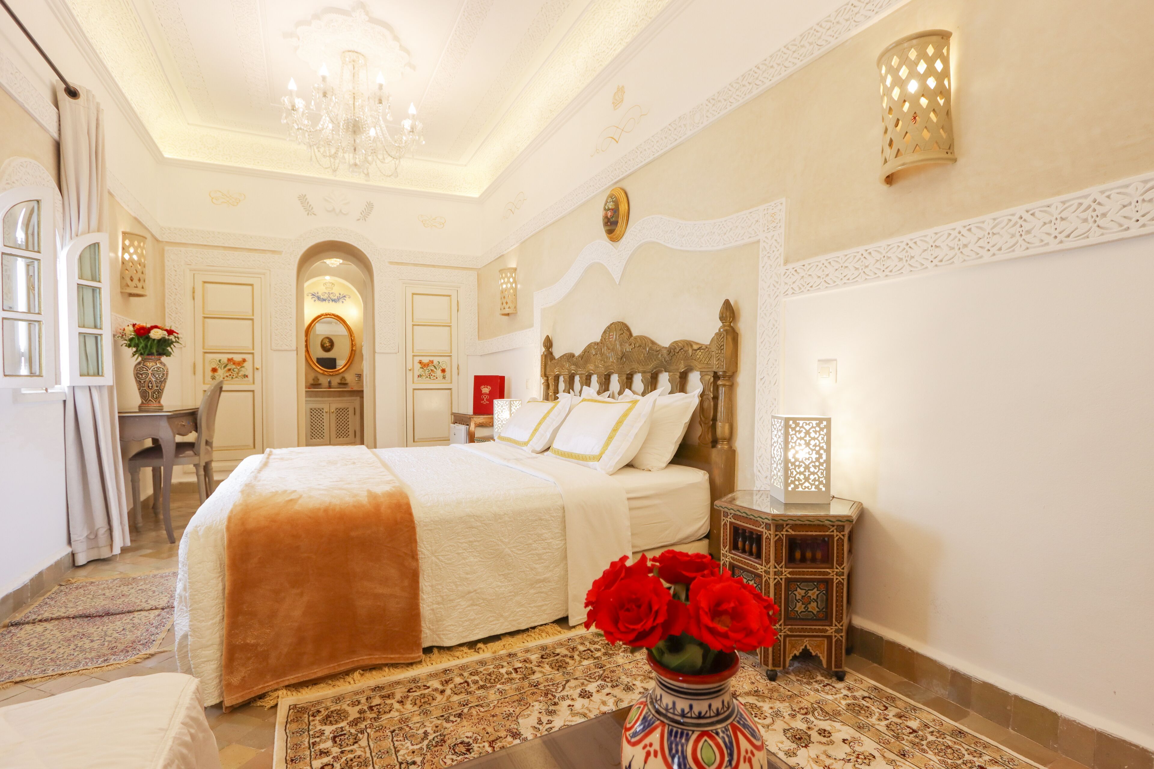 Un dormitorio elegante con una cama grande, una mesita de noche con un jarrón de rosas rojas y un panel decorativo en la pared.
