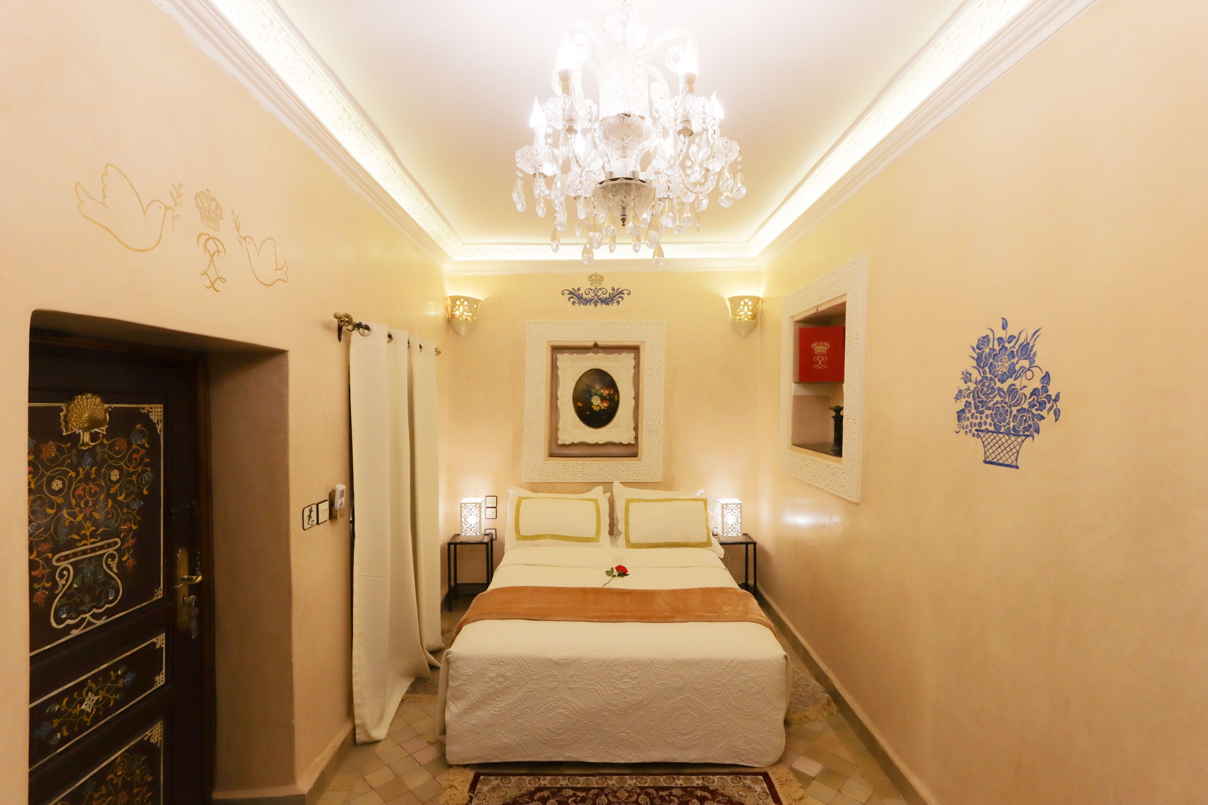 A hotel room with a bed, chandelier, decorative wall art, and a door with intricate designs.