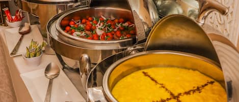 A buffet with various dishes, including a large pot of yellow rice, a bowl of salad, and a dish with tomatoes and onions.