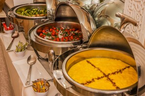 A buffet with various dishes, including a large pot of yellow rice, a bowl of salad, and a dish with tomatoes and onions. - Riad Palais des Princesses (Marrakech)