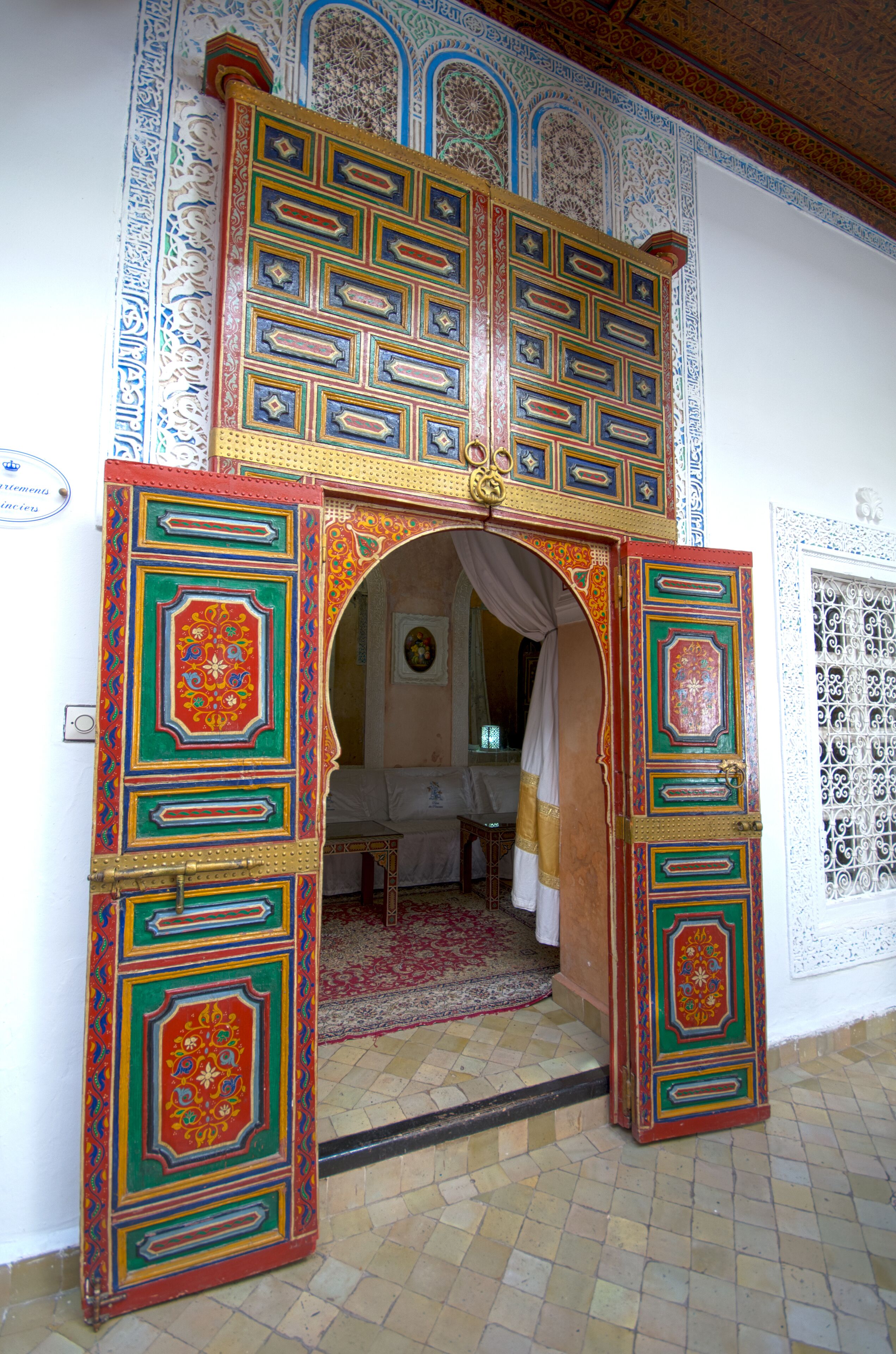 An ornate doorway with intricate designs, leading into a room with a bed and a red carpet.
