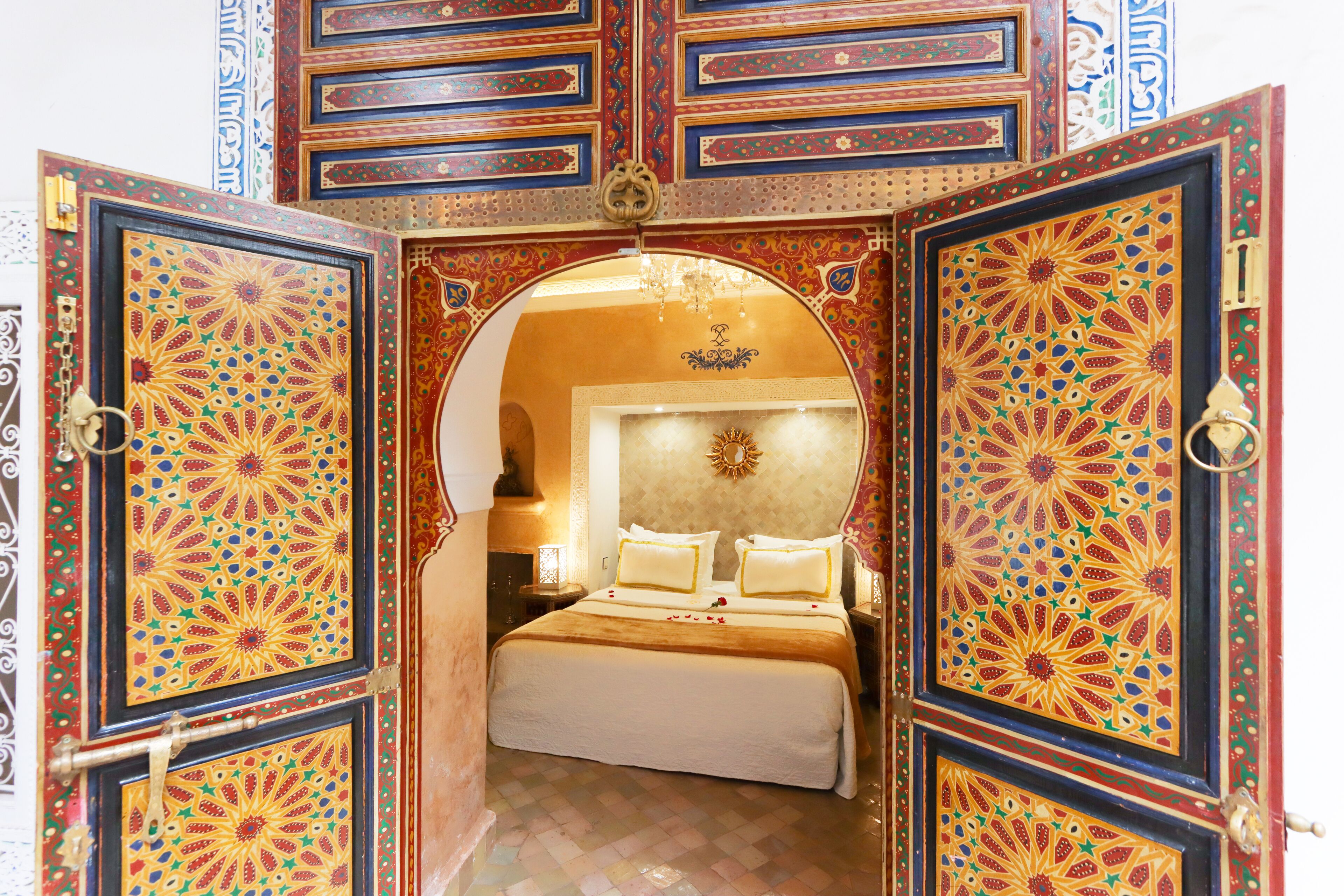 A room with a bed, a chandelier, and ornate doors with intricate patterns.