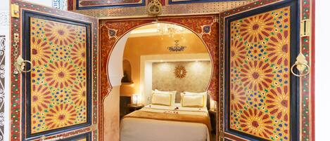 Una habitación con cama, candelabro y puertas ornamentadas con diseños elaborados.