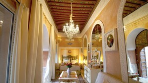 Une chambre d’hôtel luxueuse, dotée d’un lustre, d’un plafond orné et d’un lit agrémenté d’un vase de fleurs.
