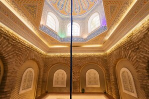 A room with intricate geometric patterns on the ceiling and walls, arched windows, and a central pillar. - Riad Palais des Princesses (Marrakech)