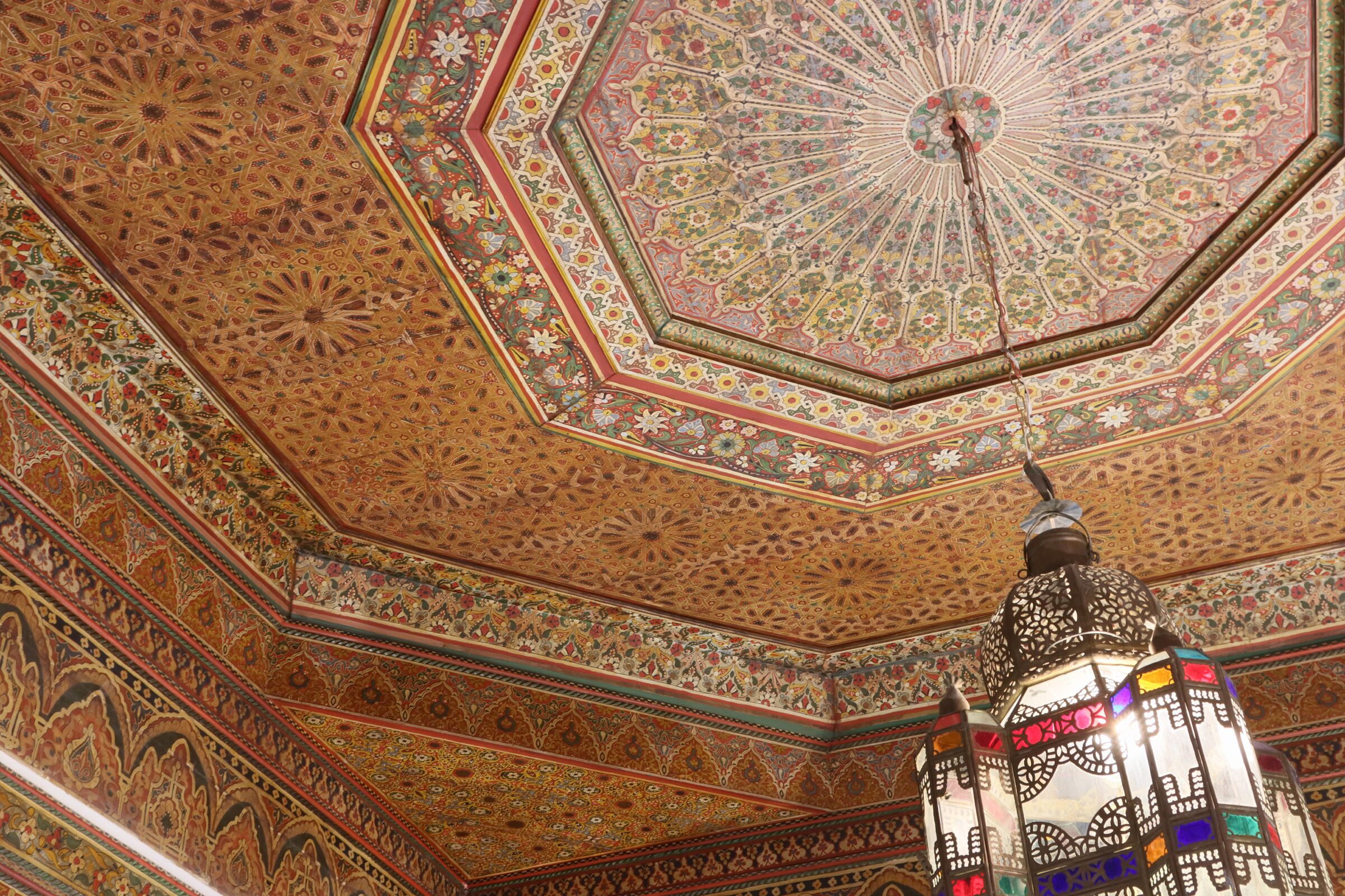 An ornate ceiling with intricate geometric patterns and a hanging lantern.