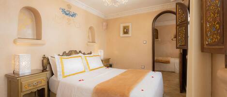 A bedroom with a large bed, a nightstand, a chandelier, and a door with intricate designs.