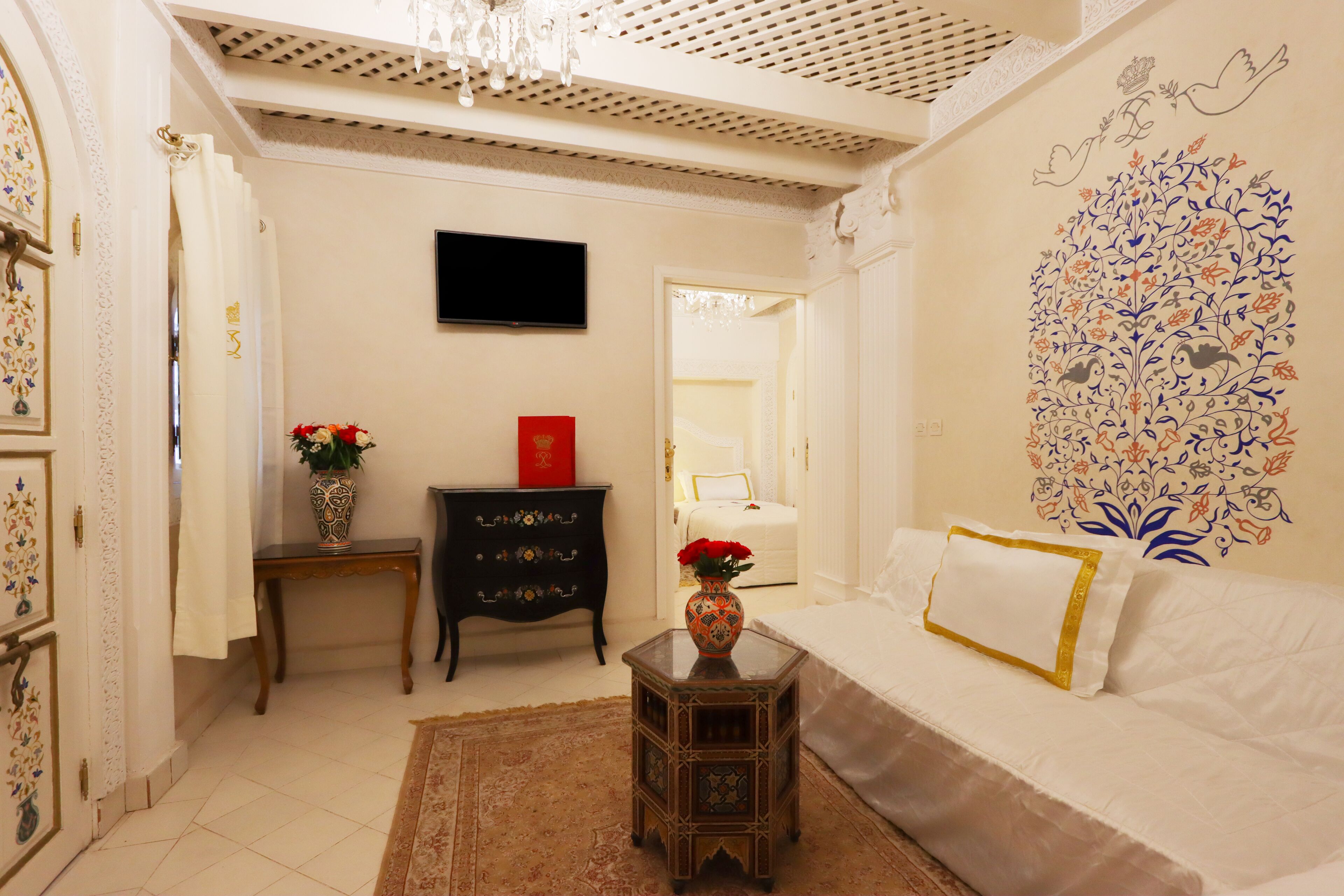 Un dormitorio con una cama, una mesita de noche con un florero, un aparador y una pared decorada con motivos florales.