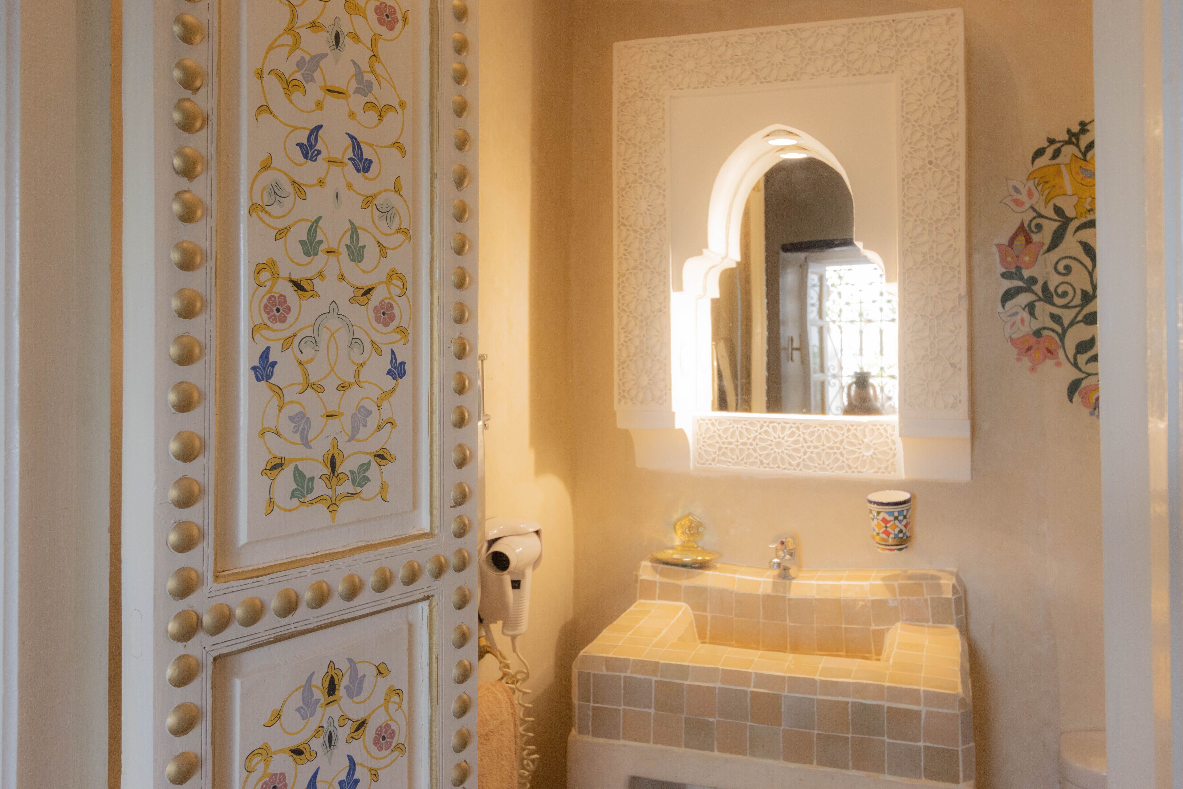 Un baño con lavamanos de azulejos, un espejo y paneles decorativos en la pared.