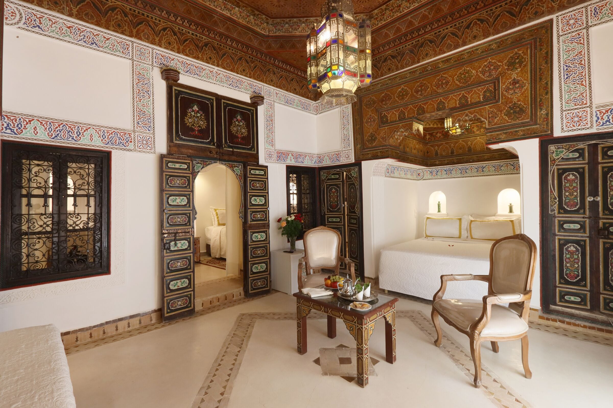 Una habitación con cama, dos sillas, una mesa y un techo decorativo.