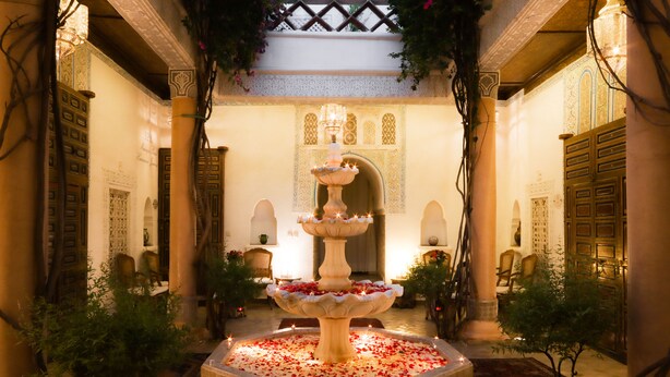 Une fontaine agrémentée d’eau et de fleurs, située dans une cour bordée de colonnes et d’arcades.