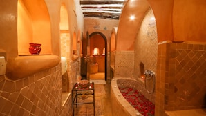 Une salle de bain luxueuse avec une grande baignoire, une petite table décorée de bougies et un arrangement floral rouge.