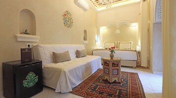 Habitación de hotel con un sofá blanco, una mesita con un jarrón, un tapete estampado y una cama con cabecero.