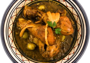 A bowl of stew with chicken, potatoes, and olives.