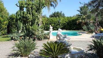Un’area piscina con una statua, circondata da diverse piante e alberi.