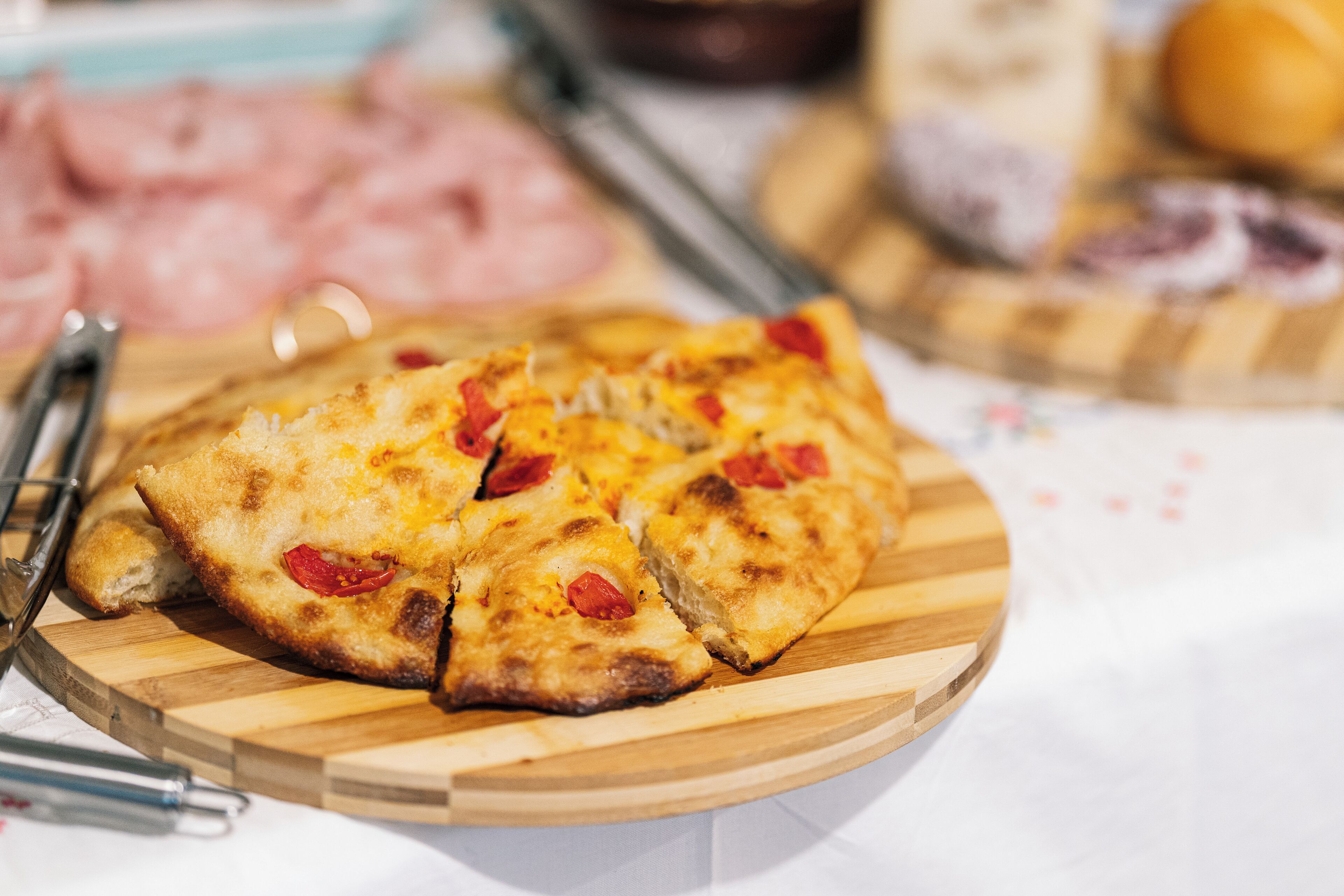 Un plato de madera con pizza cortada en porciones, acompañado de un tenedor y un cuchillo.