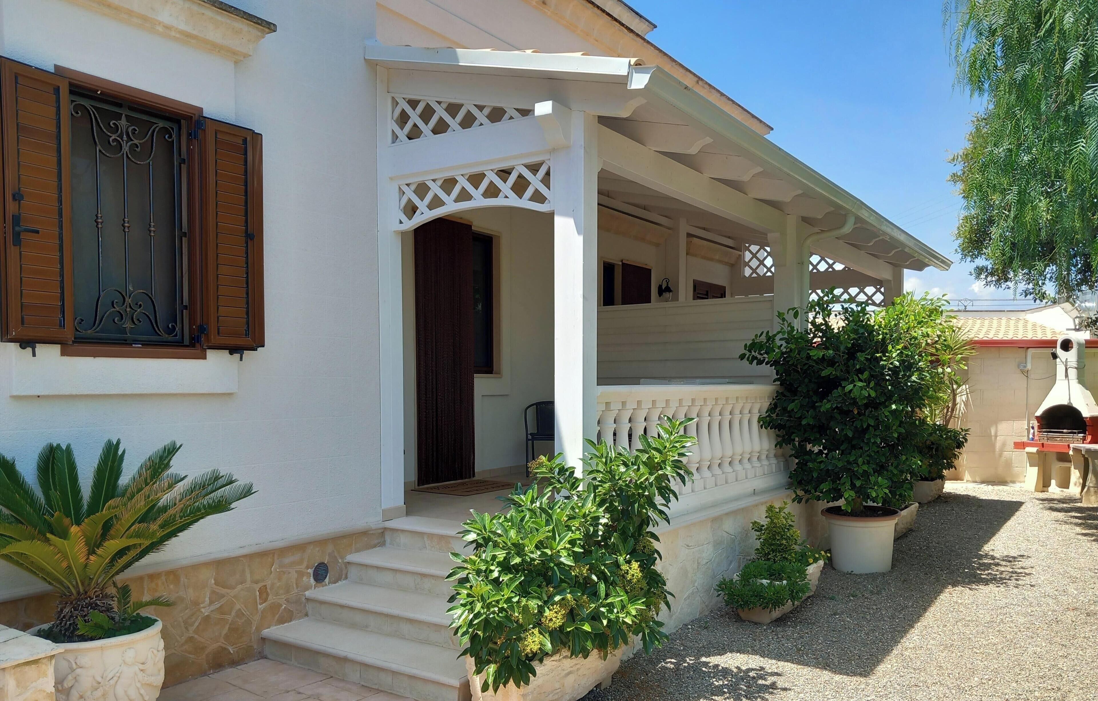 A white building with a covered porch, steps leading to the entrance, and potted plants around the area.