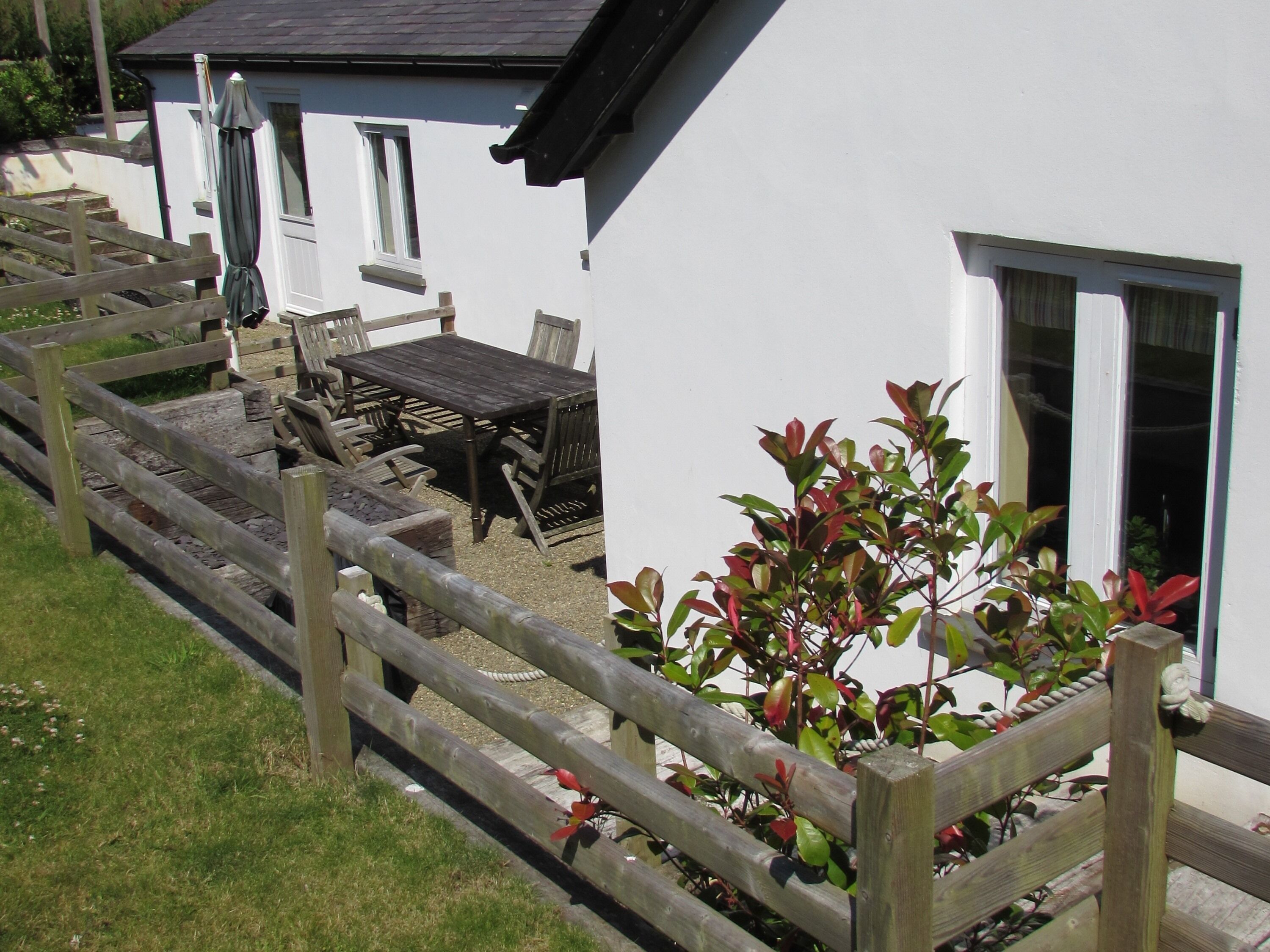 A white building with a wooden deck, a table and chairs, and a small garden area.