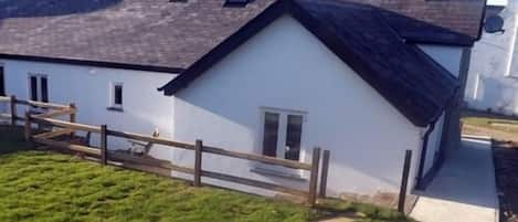 Ein weißes Gebäude mit dunklem Dach, einem Holzzaun und einer Rasenfläche davor.